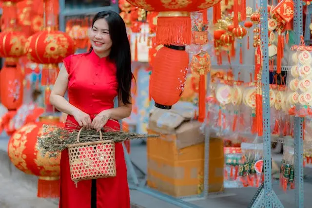 Woman wearing traditional Chinese-style red clothing while standing in a festive market decorated with red lanterns and cultural ornaments.