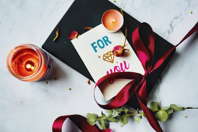Traditional wedding anniversary gift box with ribbon, candle, and greeting card on marble background